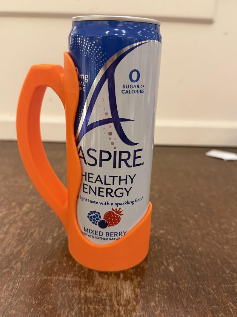 Op de afbeelding: Een oranje plastic blikhouder met een handvat, met een blikje Aspire Healthy Energy. Het blikje is blauw en wit met de woorden "Mixed Berry" en "0 Sugar or Calories" erop gedrukt.
