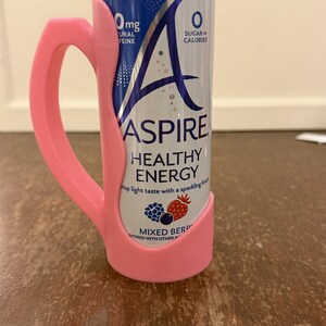 Op de afbeelding: Een roze 3D-geprinte handgreep bevestigd aan een blikje Aspire Healthy Energy. Het blikje is blauw en zilverkleurig met de woorden "Aspire Healthy Energy" en "Mixed Berry" erop gedrukt. Op het blikje staat ook "0mg Natural Caffeine" en "0 Sugar or Calories."