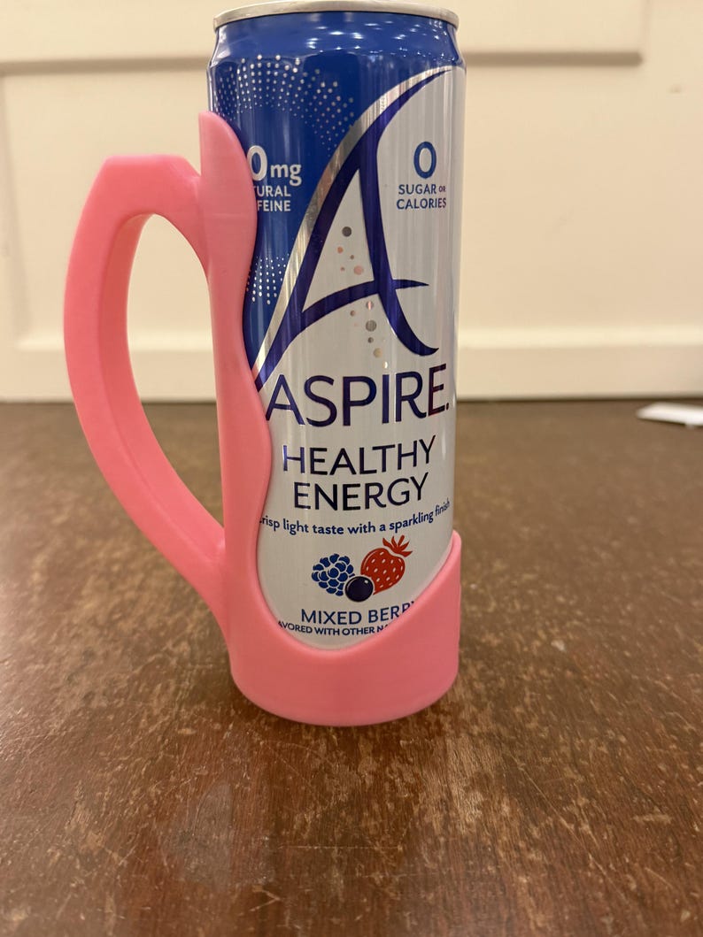 Op de afbeelding: Een roze 3D-geprinte handgreep bevestigd aan een blikje Aspire Healthy Energy. Het blikje is blauw en zilverkleurig met de woorden "Aspire Healthy Energy" en "Mixed Berry" erop gedrukt. Op het blikje staat ook "0mg Natural Caffeine" en "0 Sugar or Calories."
