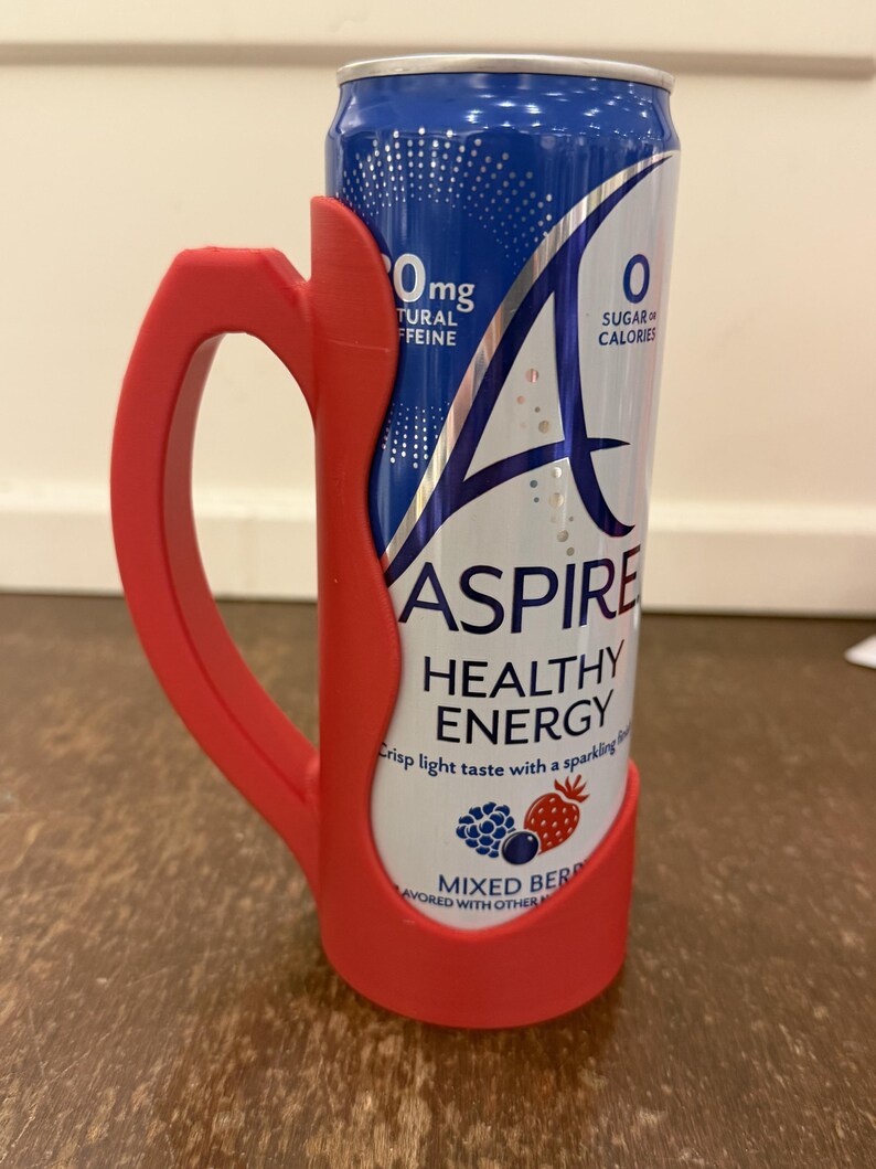 Op de afbeelding: Een rode plastic handgreep omhult een blauw en wit blikje van de drank "ASPIRE HEALTHY ENERGY". Op het blikje staat de tekst "0mg NATUURLIJKE CAFE&Iuml;NE" en "0 SUIKER CALORIE&Euml;N". Het blikje is op smaak gebracht met "MIXED BERRY".