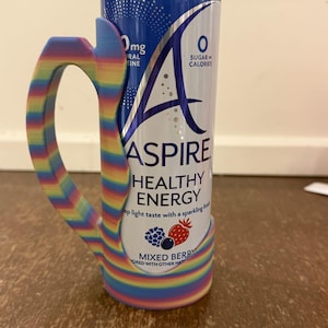 Op de afbeelding: Een blikje Aspire Healthy Energy-drank met een regenboog gestreepte handgreep. Het blikje is wit en blauw met de woorden "Aspire Healthy Energy" en "Mixed Berry" erop gedrukt. De handgreep is veelkleurig met de tekst "Spectrum Stripes".
