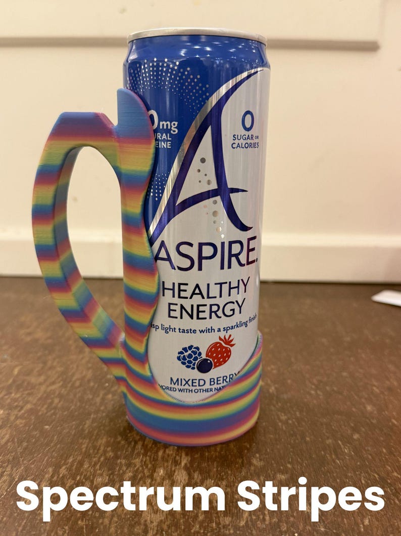 Op de afbeelding: Een blikje Aspire Healthy Energy-drank met een regenboog gestreepte handgreep. Het blikje is wit en blauw met de woorden "Aspire Healthy Energy" en "Mixed Berry" erop gedrukt. De handgreep is veelkleurig met de tekst "Spectrum Stripes".