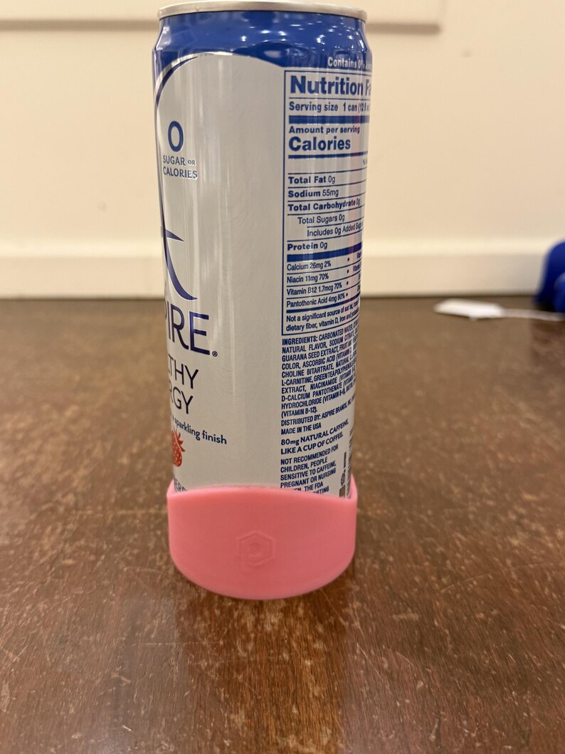 Op de afbeelding: Een zilver-blauwe Aspire Healthy Energy drankblik met een roze siliconen basis. De blik heeft voedingsfeiten en de woorden "RE" en "Healthy Energy" erop gedrukt. De basis is lichtroze en heeft een logo.