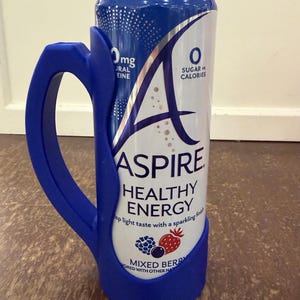 Op de afbeelding: Een blauw en wit blikje "ASPIRE HEALTHY ENERGY" met een blauwe handgreep bevestigd. Het blikje heeft de tekst "MIXED BERRY" en "0 SUGAR OR CALORIES". Het blikje is ontworpen om vastgehouden te worden met de bevestigde handgreep.