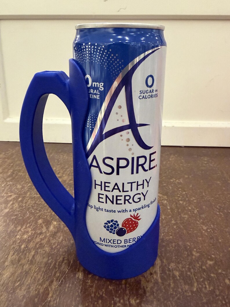 Op de afbeelding: Een blauw en wit blikje "ASPIRE HEALTHY ENERGY" met een blauwe handgreep bevestigd. Het blikje heeft de tekst "MIXED BERRY" en "0 SUGAR OR CALORIES". Het blikje is ontworpen om vastgehouden te worden met de bevestigde handgreep.