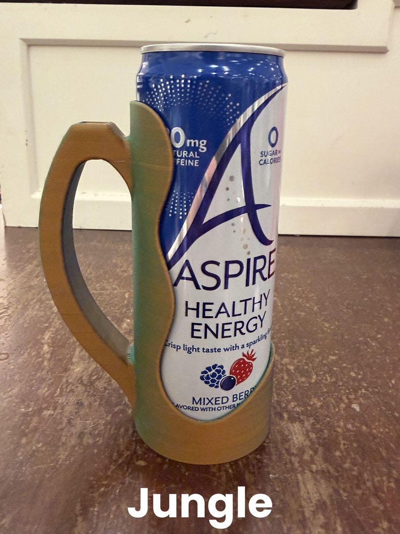 Op de afbeelding: Een blikje Aspire Healthy Energy-drank in een op maat gemaakte houder. Het blikje is wit en blauw met de tekst "Aspire Healthy Energy" en "Mixed Berry". De houder is groen en goudkleurig met het woord "Jungle" onderaan.