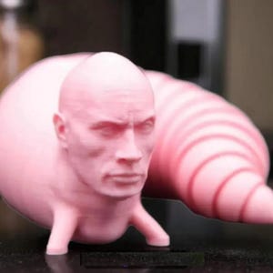 以下が含まれることがあります： 人間の頭と長いセグメント状の尾を持つピンクの3Dプリント彫刻。頭は真剣な表情をしていて、尾は丸まっています。