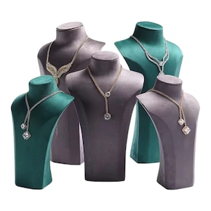 May include: A collection of jewelry display busts in various colors, including green and gray. Each bust showcases a different necklace with sparkling gemstones. The necklaces feature various designs, including lariat and pendant styles, perfect for showcasing jewelry.
