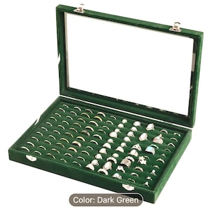 May include: Dark green velvet ring box with a glass lid. The box is filled with rows of silver rings.