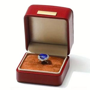 May include: A blue heart-shaped sapphire ring with a diamond halo setting, displayed in a red velvet ring box.