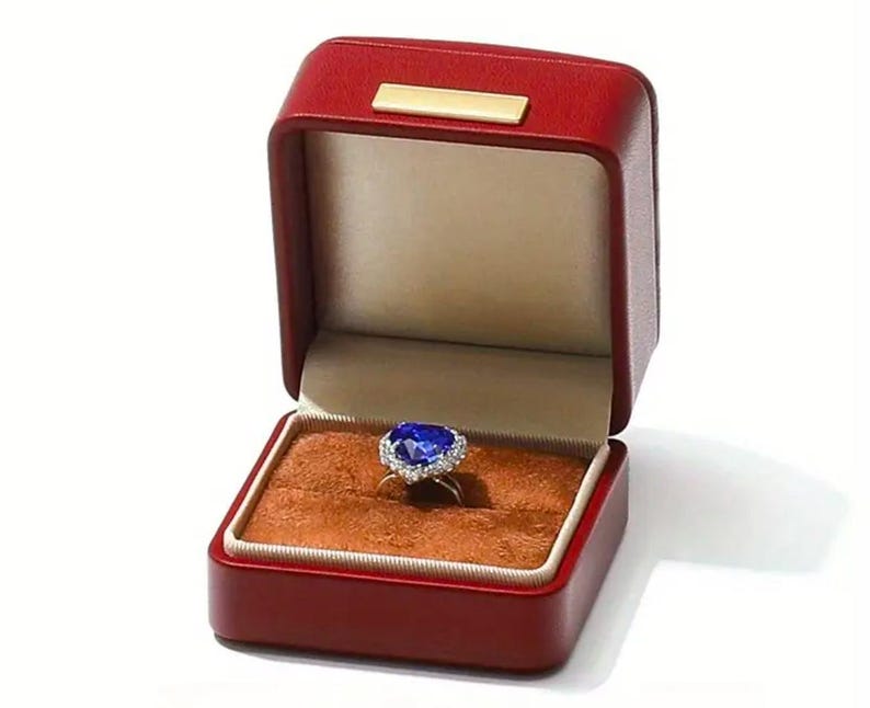 May include: A blue heart-shaped sapphire ring with a diamond halo setting, displayed in a red velvet ring box.