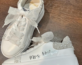 May include: White platform sneakers with pearl embellishments and a white tulle bow. The sneakers have the text "Mrs. Halpern" written on the side.