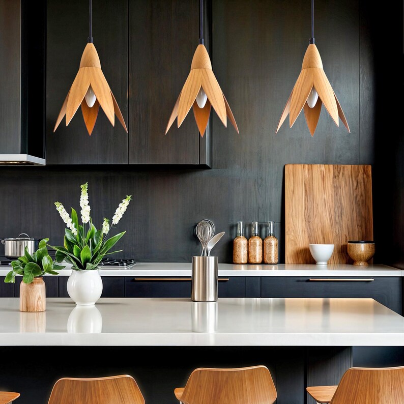 Three modern kitchen pendant lights with a minimalist design. Each light features a light brown, wood-like, tulip-shaped shade hanging from a black cord. The lights are shown hanging above a kitchen counter with dark cabinetry and a white countertop.  The overall style is contemporary and sleek.