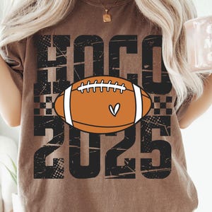 May include: Brown t-shirt with the text "HOCO 2025" in black, featuring a football graphic with a heart. The shirt also has SVG, PNG, EPS, and DXF text. The shirt is a casual style.