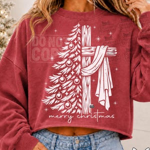 May include: A red long-sleeve cropped sweatshirt featuring a white graphic of a Christmas tree merged with a wooden cross draped in fabric. The text "merry christmas" is printed below the graphic in a white script font.