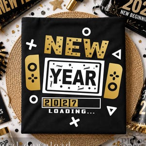 May include: A black t-shirt featuring a gold and white graphic of a handheld gaming console. The text reads NEW YEAR with 2027 LOADING below it. The design includes geometric shapes like circles, triangles, and plus signs on a black background.