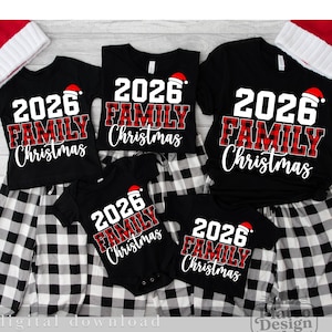 Könnte beinhalten: Eine Auswahl an schwarzen Kurzarmshirts und einem Babybody mit dem weißen Text 2026, dem Wort FAMILY in rot-schwarzem Schottenkaro und dem Wort Christmas in weißer Schreibschrift, jeweils verziert mit einer kleinen rot-weißen Weihnachtsmütze.
