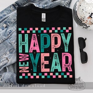 Pu&ograve; includere: Una t-shirt nera con la scritta HAPPY NEW YEAR in un carattere usurato e testurizzato con lettere alternate rosa e turchese. Il design include un bordo a scacchi rosa e turchese nella parte superiore e inferiore, decorato con piccole stelle.