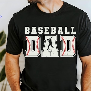 Puede incluir: Camiseta negra con el texto "Baseball Dad" en blanco con un gráfico de béisbol. El gráfico de béisbol es rojo y blanco con una silueta de un jugador de béisbol golpeando una pelota.