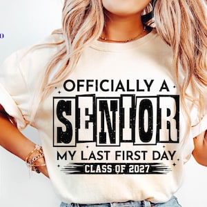 May include: Cream-colored t-shirt with the text "OFFICIALLY A SENIOR" in a bold, black font. Below it reads "MY LAST FIRST DAY. CLASS OF 2027." The shirt also features SVG, PNG, EPS, and DXF file type logos.