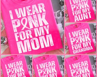 May include: A bright pink t-shirt featuring the white distressed text I WEAR PINK FOR MY MOM with a breast cancer awareness ribbon replacing the letter I in PINK. The shirt has a crew neckline and is made of a soft, solid-colored cotton fabric.