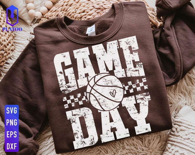 Puede incluir: Una sudadera marr&oacute;n con la frase "GAME DAY" en blanco desgastado. Un gr&aacute;fico de baloncesto con un coraz&oacute;n est&aacute; centrado entre las palabras. La sudadera es de cuello redondo.