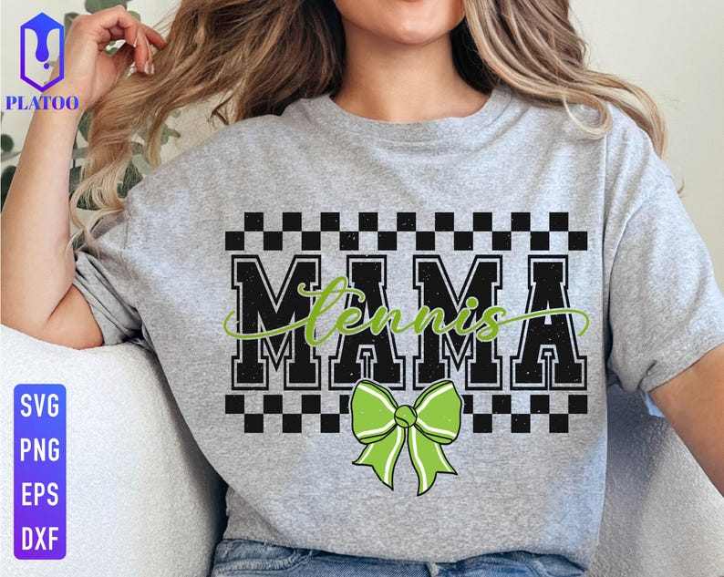 May include: A light gray t-shirt with the word "MAMA" in a bold, black, block font, with "Tennis" in a green script font. A green bow is below the text. The shirt has a checkered pattern above the word "MAMA".