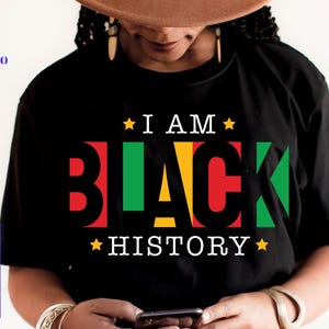 May include: Black t-shirt with the text "I AM BLACK HISTORY" in red, green, yellow, and white. The design includes stars and is a statement piece for celebrating Black history and culture.