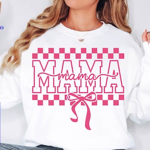 May include: White sweatshirt with a pink checkered design and the word "MAMA" in a bold, pink font. A pink bow is below the word. The sweatshirt also has the text "SVG PNG EPS DXF" in a blue box.