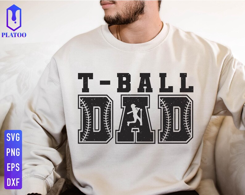 Puede incluir: Sudadera color crema con el texto "T-BALL DAD" en una fuente negra y audaz, desgastada. Las letras "D" y "A" est&aacute;n dise&ntilde;adas con costuras de b&eacute;isbol y una silueta de jugador de b&eacute;isbol. La sudadera es de estilo casual.