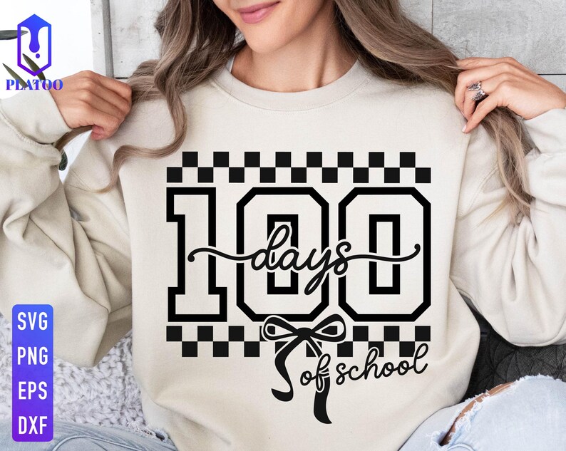 May include: A beige sweatshirt with a black graphic that reads "100 days of school." The number 100 is in a bold, blocky font, with the word "days" in a cursive script. A bow is below the word "days".
