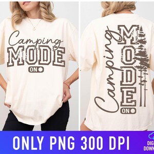 May include: Cream-coloured t-shirt with the text "Camping MODE ON" in brown, distressed lettering on the front. The back of the shirt features the words "Camping MODE ON" vertically and a tree graphic.