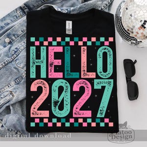 Pu&ograve; includere: Una t-shirt nera con la scritta HELLO 2027 in un carattere usurato e testurizzato con colori alternati turchese e rosa. Il design include un bordo a scacchi nella parte superiore e inferiore e piccoli accenti a stella nelle lettere.