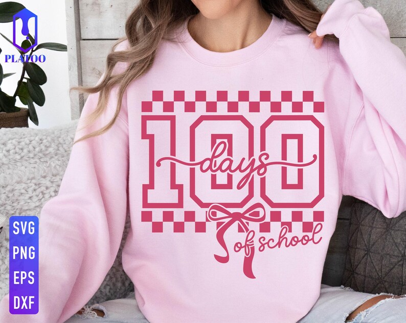 May include: A light pink sweatshirt with a graphic design in a darker shade of pink. The design features the number "100" with the words "days of school" in a script font, and a bow. The sweatshirt is a crew neck style.
