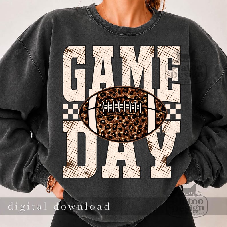 May include: A charcoal gray crewneck sweatshirt featuring a large graphic print with the text "GAME DAY" in a beige, dotted pattern. Centered between the words is a football illustration with a brown and black leopard print texture.
