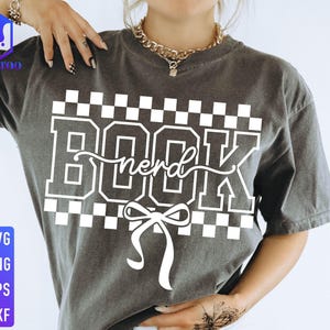 May include: Dark gray t-shirt with the words "BOOK nerd" in white block letters and a white bow. The word "nerd" is in a cursive font. The shirt has a checkered pattern above and below the text. The shirt also has the words "SVG, PNG, EPS, DXF" in blue and white.