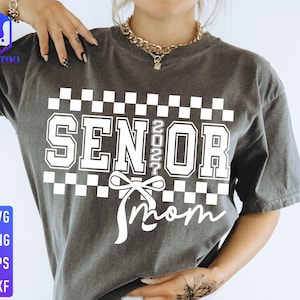 May include: Dark gray t-shirt with the words "SENIOR 2022 Mom" in white block letters and a bow graphic. The shirt has a checkered pattern above the text. The lower left corner has the text "SVG PNG EPS DXF".