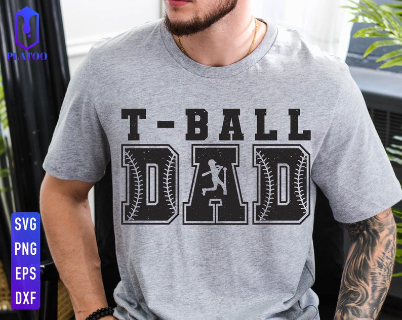 Puede incluir: Una camiseta gris con el texto "T-BALL DAD" en fuente negra desgastada. La palabra "DAD" presenta un dise&ntilde;o de b&eacute;isbol con una silueta de bateador. La camiseta es de estilo casual.