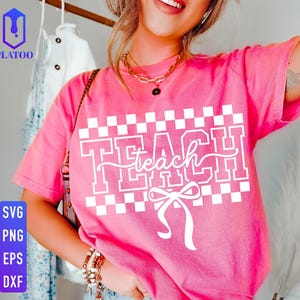 May include: A pink t-shirt with the word "TEACH" in white, featuring a bow and a checkered pattern. The shirt is a vibrant pink color and has short sleeves. The image also includes the words "SVG, PNG, EPS, DXF".