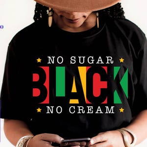 Peut inclure: T-shirt noir avec l'inscription "NO SUGAR BLACK NO CREAM" en blanc, rouge, vert et jaune. Le mot "BLACK" est en grandes lettres grasses. Le t-shirt a un col rond et des manches courtes.