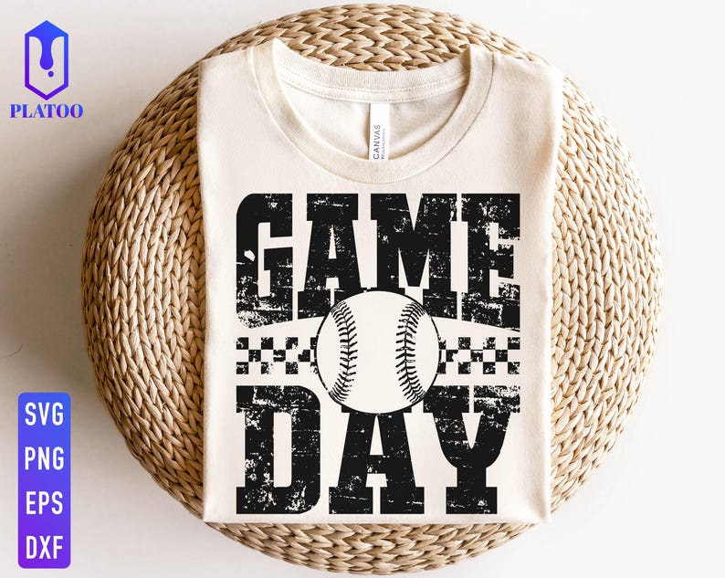 May include: A cream-coloured t-shirt with the words "GAME DAY" in distressed black lettering, featuring a baseball graphic. The shirt is displayed on a woven, circular surface. The shirt is a baseball-themed item.