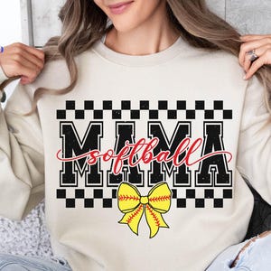 May include: A white sweatshirt with a black and white checkered design. The text "Mama Softball" is written in black with a red "softball" and a yellow and red bow.