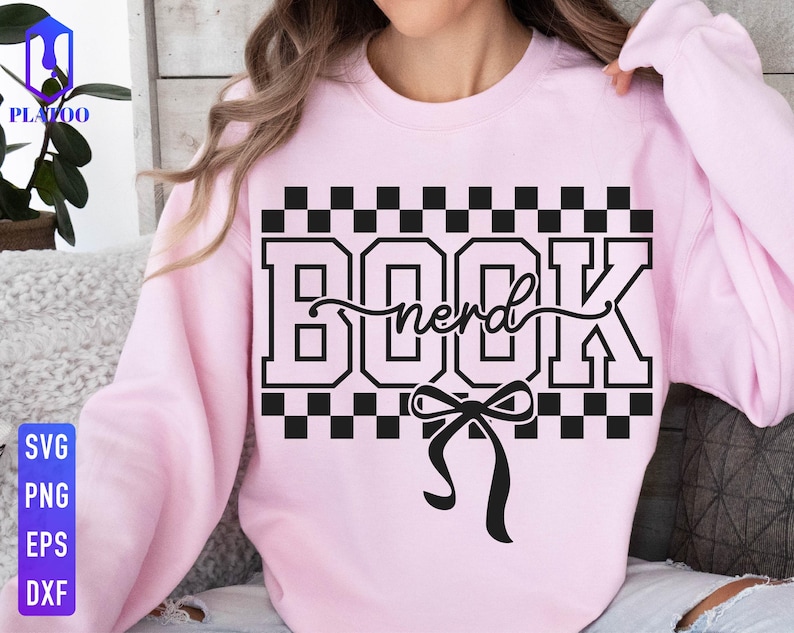 May include: A light pink sweatshirt with a black and white checkered design and the words "BOOK nerd" in a bold font. A black bow is below the text. The sweatshirt is a casual style.