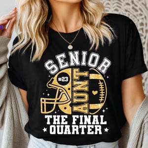 May include: Black t-shirt with a gold football and helmet design. Text reads "SENIOR AUNT #23 THE FINAL QUARTER". The shirt is a casual style, suitable for game day or everyday wear.