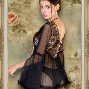 May include: A black sheer top with lace detailing and a ruffled hem. The top is worn over a black bra and underwear. The model is standing in front of a floral background.