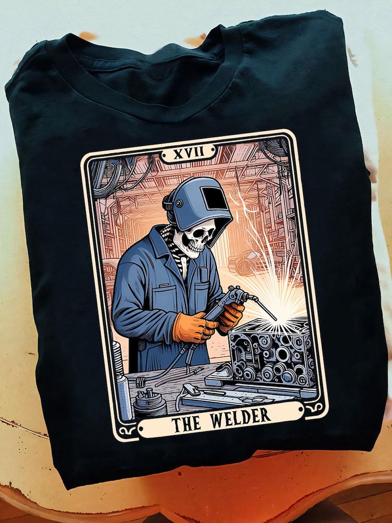 May include: A black t-shirt with a tarot card design featuring a skeleton welding a metal part. The card is labeled "XVII The Welder".