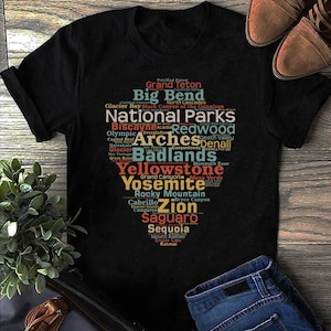 Könnte beinhalten: Ein schwarzes T-Shirt mit einem bunten Wortwolken-Design, das die Namen verschiedener Nationalparks in den Vereinigten Staaten zeigt. Der Text enthält "National Parks", "Yellowstone", "Yosemite", "Zion", "Grand Canyon", "Acadia", "Redwood", "Arches", "Badlands" und mehr.