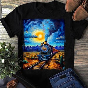 May include: Black t-shirt featuring a vibrant painting of a steam train traveling through a desert landscape under a bright sun. The artwork includes blue, orange, and yellow hues, with a detailed depiction of the train and its surroundings.