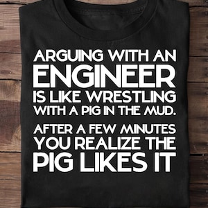 Peut inclure: T-shirt noir avec texte blanc : "ARGUER AVEC UN INGÉNIEUR, C'EST COMME LUTTER AVEC UN COCHON DANS LA BOUE. APRÈS QUELQUES MINUTES, VOUS RÉALISEZ QUE LE COCHON AIME ÇA."
