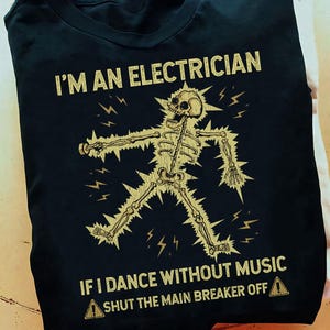 Puede incluir: Camiseta negra con un gráfico de un esqueleto bailando con rayos. El texto dice "Soy electricista. Si bailo sin música, apaga el interruptor principal."